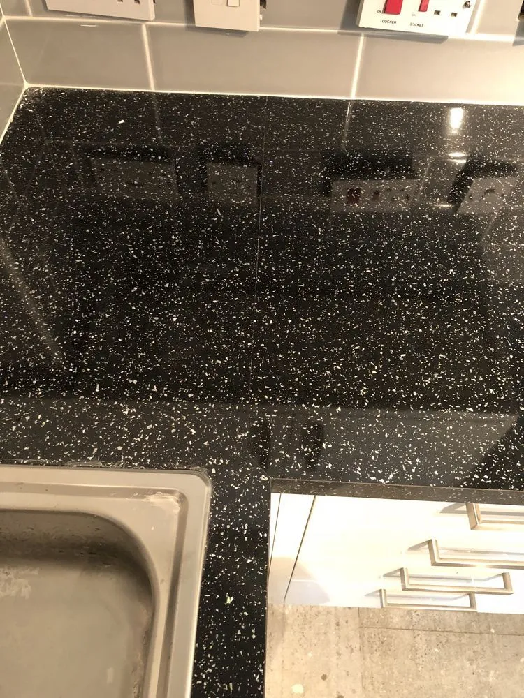 Close-up of polished black granite worktop with stainless steel sink and concrete-look flooring in a finished Bedminster kitchen